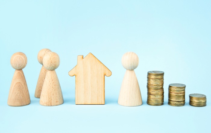 Grundsteuerreform 2025. Holzhaus und kleine Holzfiguren vor blauem Hintergrund. Vermögensaufteilung.